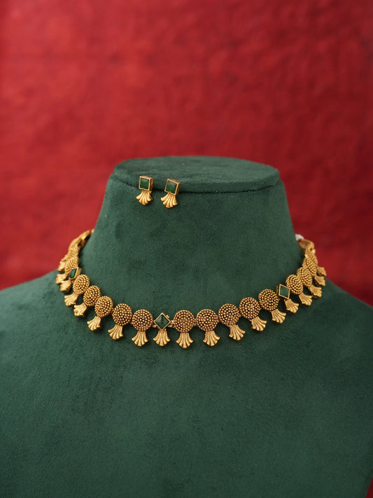 Gold-toned traditional necklace and matching rectangular stud earrings displayed on a dark green velvet jewelry bust against a textured red background.