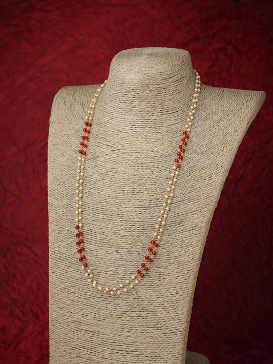A long strand necklace with small cream pearls and alternating red faceted beads, displayed on a beige fabric-covered jewelry bust against a dark red textured background.