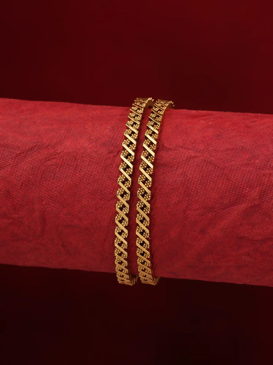 Two gold-toned chain bracelets displayed on a textured red cylindrical stand against a dark red background.