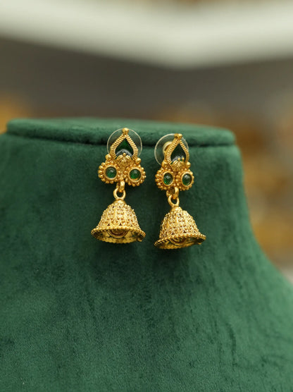 A pair of gold-toned traditional jhumka earrings with green stone accents, displayed on a dark green velvet jewelry bust.