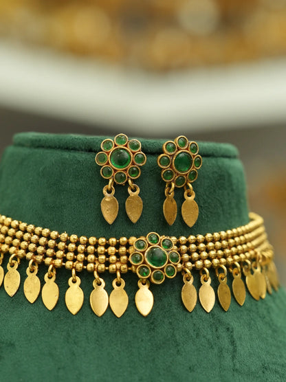 Gold-toned traditional jewelry set featuring a beaded necklace and matching earrings with green stone accents, displayed on a dark green velvet jewelry stand.
