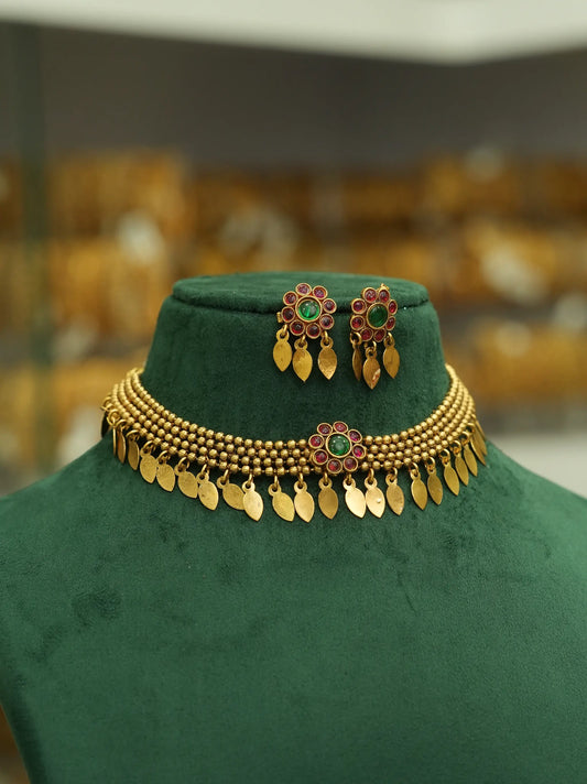 Gold-tone jewelry set displayed on a dark green velvet mannequin bust, featuring a beaded necklace with hanging leaf-shaped charms, matching earrings, and a decorative piece with red and green floral details.