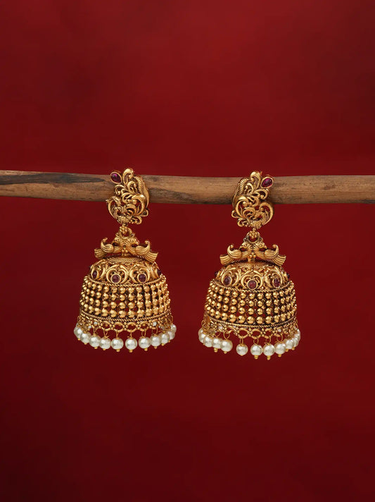 Gold-toned peacock jhumka earrings with pearl drops, front view, displayed on a wooden stand against a maroon background