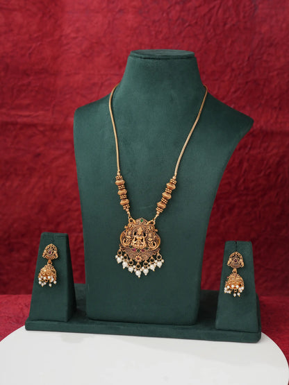 Gold-toned traditional Indian jewelry set featuring a necklace and matching earrings displayed on a dark green velvet jewelry bust against a textured red background.
