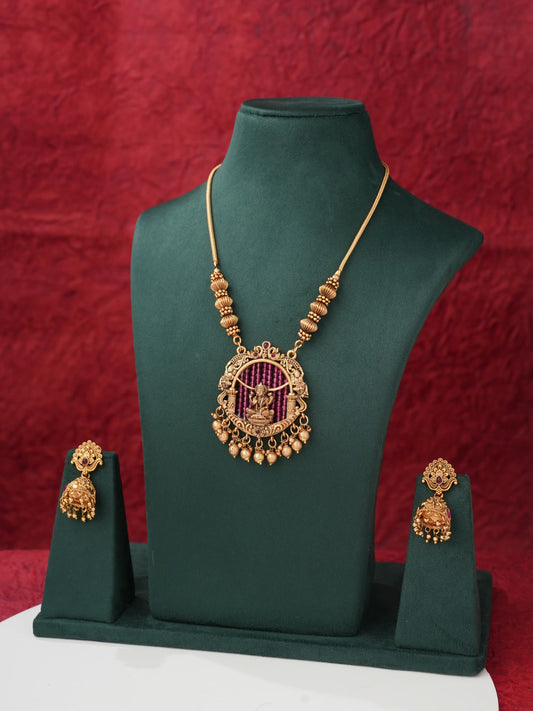 Gold-toned jewelry set displayed on a dark green mannequin bust, featuring a necklace with a circular pendant and matching earrings, set against a textured red backdrop.