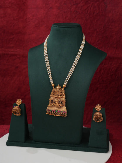 Gold-toned traditional necklace and matching earrings displayed on a dark green jewelry bust against a deep red textured backdrop.