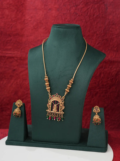 Gold-toned traditional Indian jewelry set featuring a necklace with a birdcage pendant and matching earrings, displayed on a dark green jewelry bust against a textured red background.
