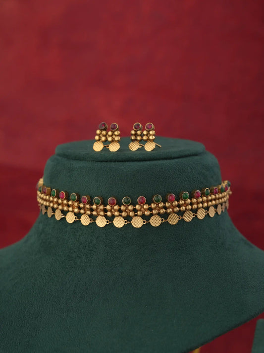 Gold-toned traditional necklace and matching earrings displayed on a dark green velvet jewelry bust against a textured red background.