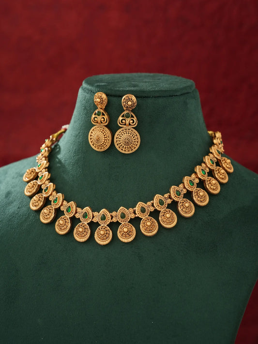 Gold-toned traditional jewelry set including a coin-style necklace and matching earrings, displayed on a dark green velvet mannequin bust against a deep red background.