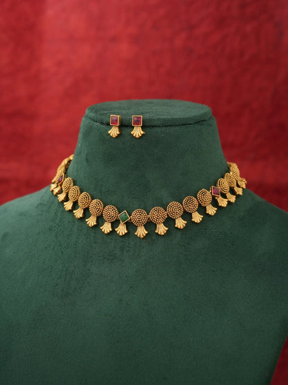 Gold-toned traditional necklace and matching stud earrings displayed on a dark green velvet jewelry bust against a textured red background.