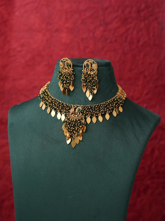 Gold-toned traditional jewelry set featuring a necklace and matching earrings displayed on a dark green velvet mannequin bust against a textured red background.