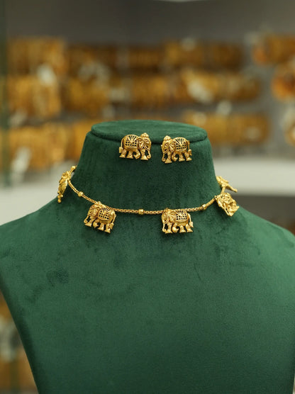 Gold elephant jewelry set including a necklace and matching earrings displayed on a dark green velvet jewelry bust, with a blurred shop background.