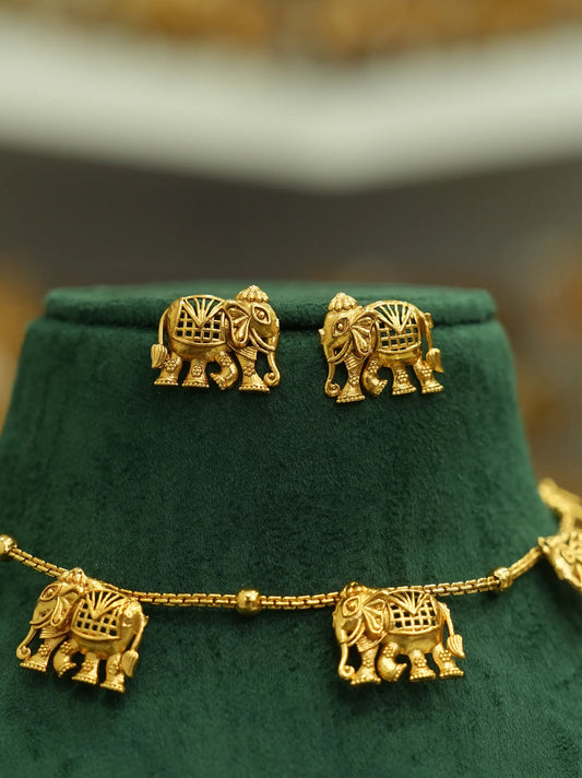 Gold elephant jewelry set displayed on a dark green velvet jewelry bust, featuring a necklace and matching stud earrings.