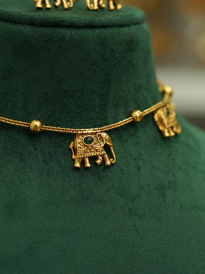 Gold-toned elephant pendant necklace with a small green stone detail, displayed on a dark green velvet jewelry bust.