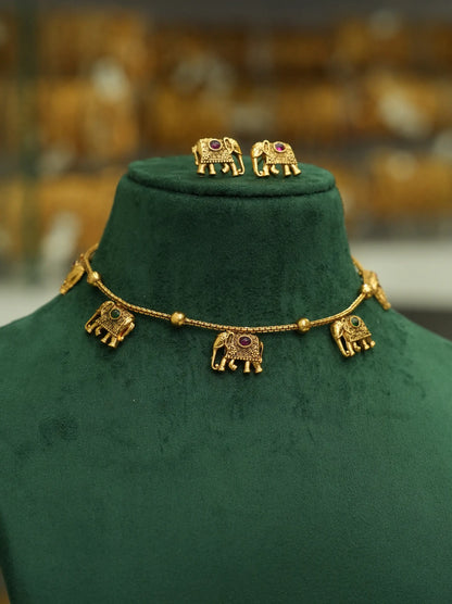 Gold elephant jewelry set displayed on a dark green velvet mannequin bust, featuring a necklace with five small elephant charms and matching stud earrings.