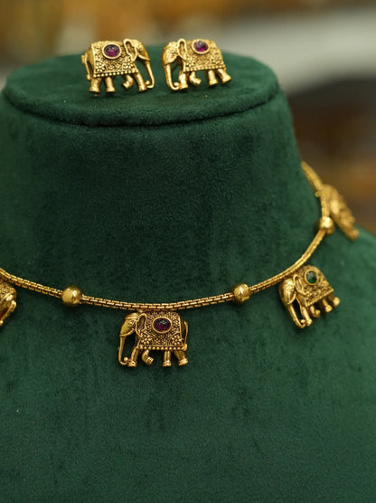 Gold-toned jewelry set displayed on a dark green velvet jewelry bust, featuring a necklace with elephant charms and matching stud earrings.