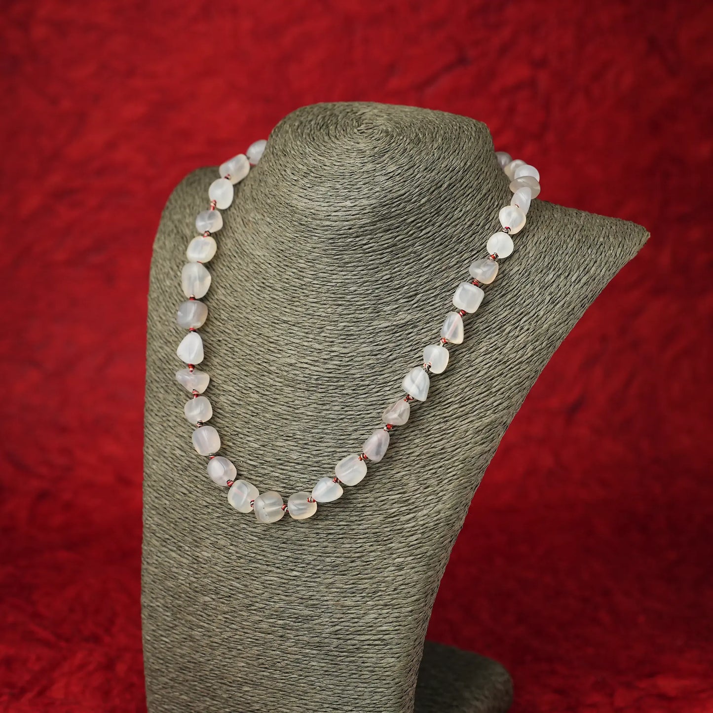 White stone beaded necklace displayed on a grey neck form against a dark red background.