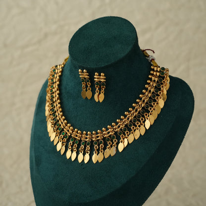 Gold-toned traditional necklace and matching drop earrings displayed on a dark green velvet jewelry bust against a light textured wall.