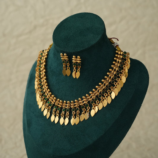 Gold-toned traditional necklace and matching drop earrings displayed on a dark green velvet jewelry bust against a light textured wall.