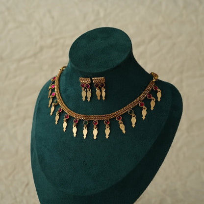 Gold-toned traditional jewelry set including a necklace and matching earrings displayed on a dark green velvet jewelry bust against a light textured background.