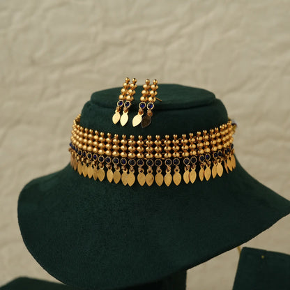 Gold-toned traditional jewelry set displayed on a dark green velvet mannequin bust, featuring a wide beaded and coin-leaf choker necklace with matching drop earrings.