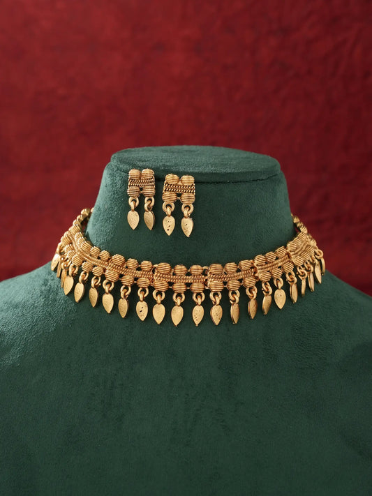 Gold-toned traditional necklace and matching drop earrings displayed on a dark green velvet jewelry bust against a textured red background.