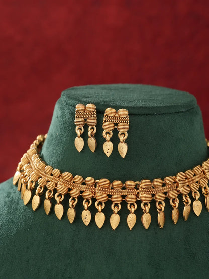Gold-toned traditional jewelry set featuring a multi-strand necklace with dangling leaf-shaped charms and matching drop earrings, displayed on a dark green velvet mannequin bust against a textured red background.