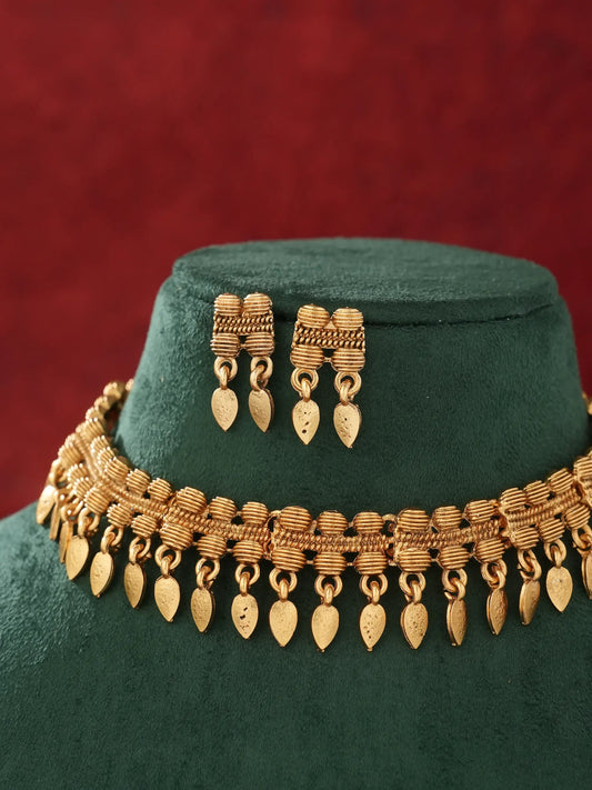 Gold-toned traditional jewelry set featuring a multi-strand necklace with dangling leaf-shaped charms and matching drop earrings, displayed on a dark green velvet mannequin bust against a textured red background.