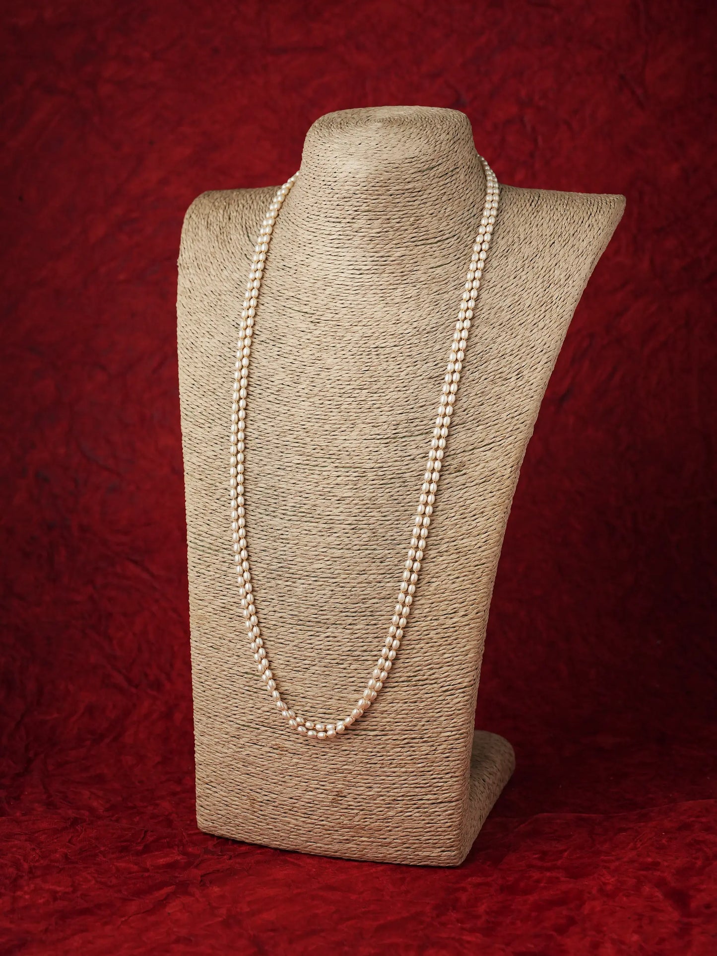 Long double-strand pearl chain necklace displayed on a beige neck form against a dark red background.