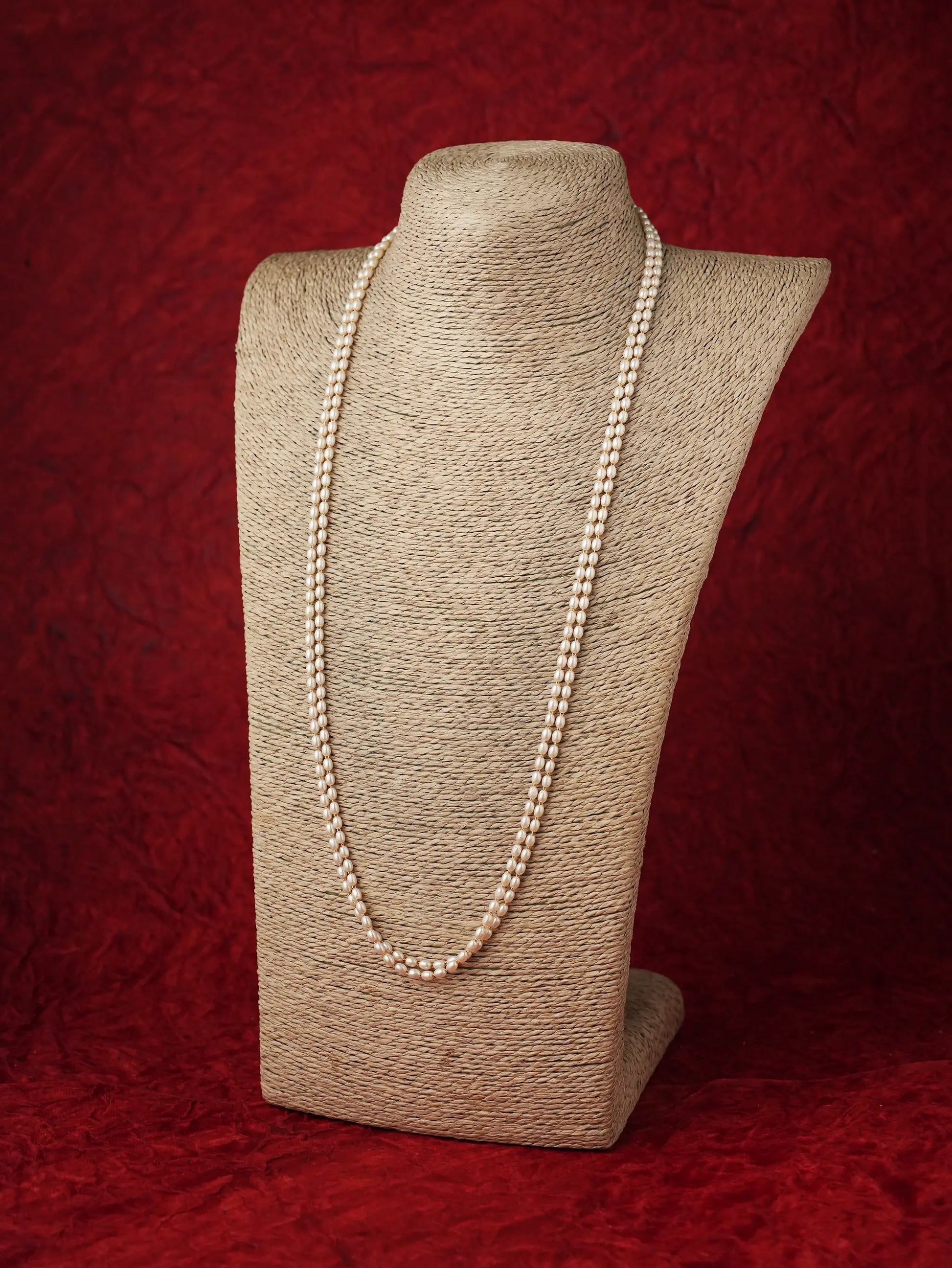 Long double-strand pearl chain necklace displayed on a beige neck form against a dark red background.