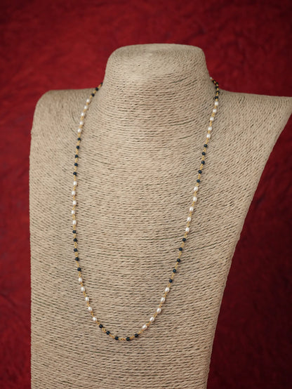 A long beaded necklace displayed on a textured beige fabric mannequin bust against a dark red background. The necklace features alternating strands of small white pearls and dark Blue beads separated by tiny metallic spacer beads.