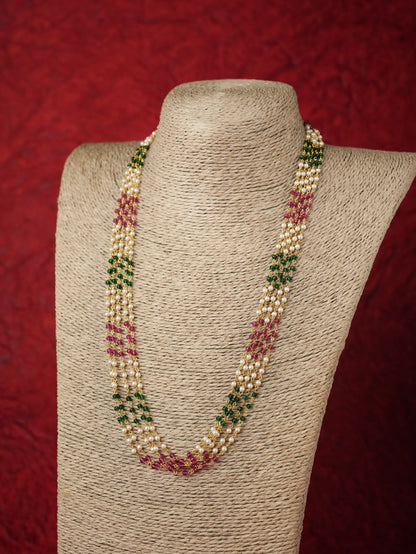 A multi-strand beaded necklace displayed on a textured beige fabric mannequin bust against a dark red background. The necklace features cream-colored beads, green beads, and pink beads woven together in a patterned design.