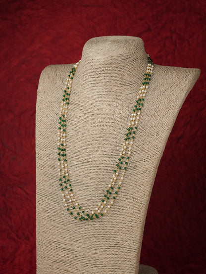 A multi-strand pearl necklace with green stone accents, displayed on a beige fabric-covered jewelry bust against a textured dark red background.