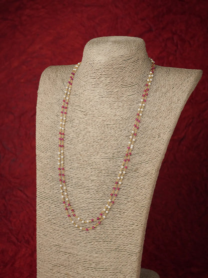 A long strand necklace with alternating cream pearls and small pink beads, displayed on a beige fabric-covered jewelry bust against a textured dark red background.