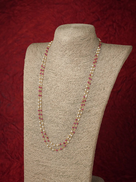A long strand necklace with alternating cream pearls and small pink beads, displayed on a beige fabric-covered jewelry bust against a textured dark red background.