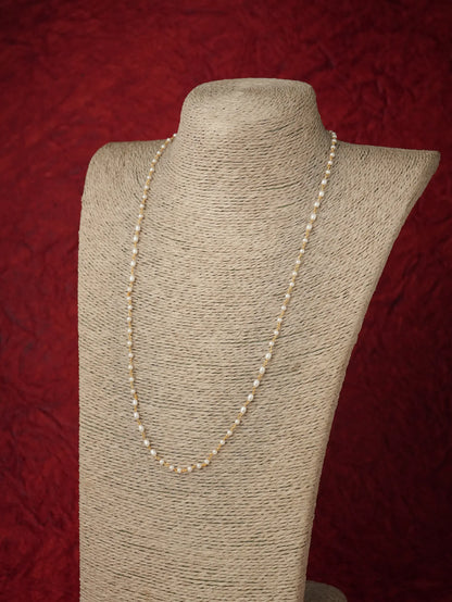 A long strand of cream-colored seed pearls displayed on a beige fabric-covered jewelry bust against a textured dark red background.