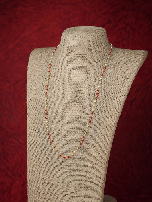 A beaded necklace with alternating cream beads and small red beads, displayed on a textured beige fabric mannequin bust against a dark red textured background.