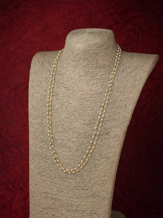 A long strand of cream-colored pearls draped over a beige fabric-covered jewelry display bust against a dark red textured background.