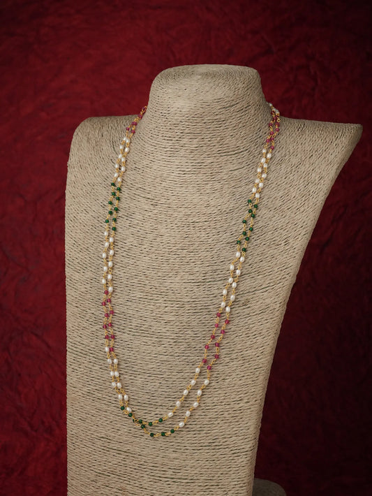 A double-strand pearl necklace with small green and red bead accents, displayed on a beige fabric-covered jewelry bust against a dark red textured background.
