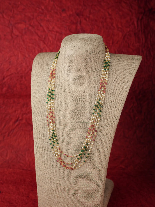 A multi-strand beaded necklace displayed on a beige fabric-covered jewelry bust against a textured red background. The necklace features strands of cream beads, light pink beads, and dark green beads.