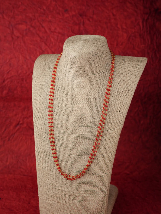 A beaded necklace made of small orange-red beads, displayed on a beige fabric-covered jewelry bust against a textured red background.
