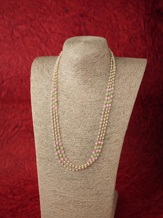 A long double-strand pearl necklace with small pink and green bead accents, displayed on a beige fabric-covered jewelry bust against a textured red background.